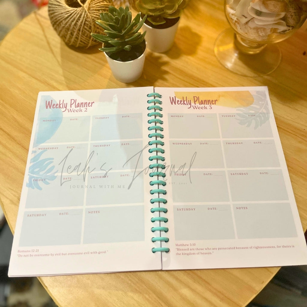 Open weekly planner on a wooden table with plants and a glass in the background