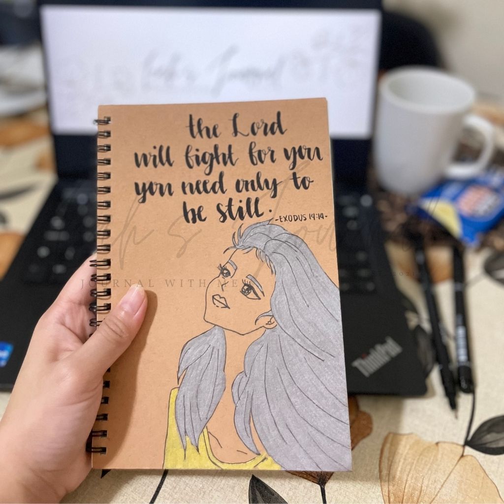 Notebook with a motivational quote and illustration held by a hand, with a blurred office background.