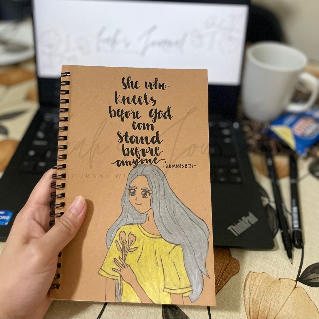 Notebook with illustration and text held by a hand on a desk with a laptop and coffee cup in the background.