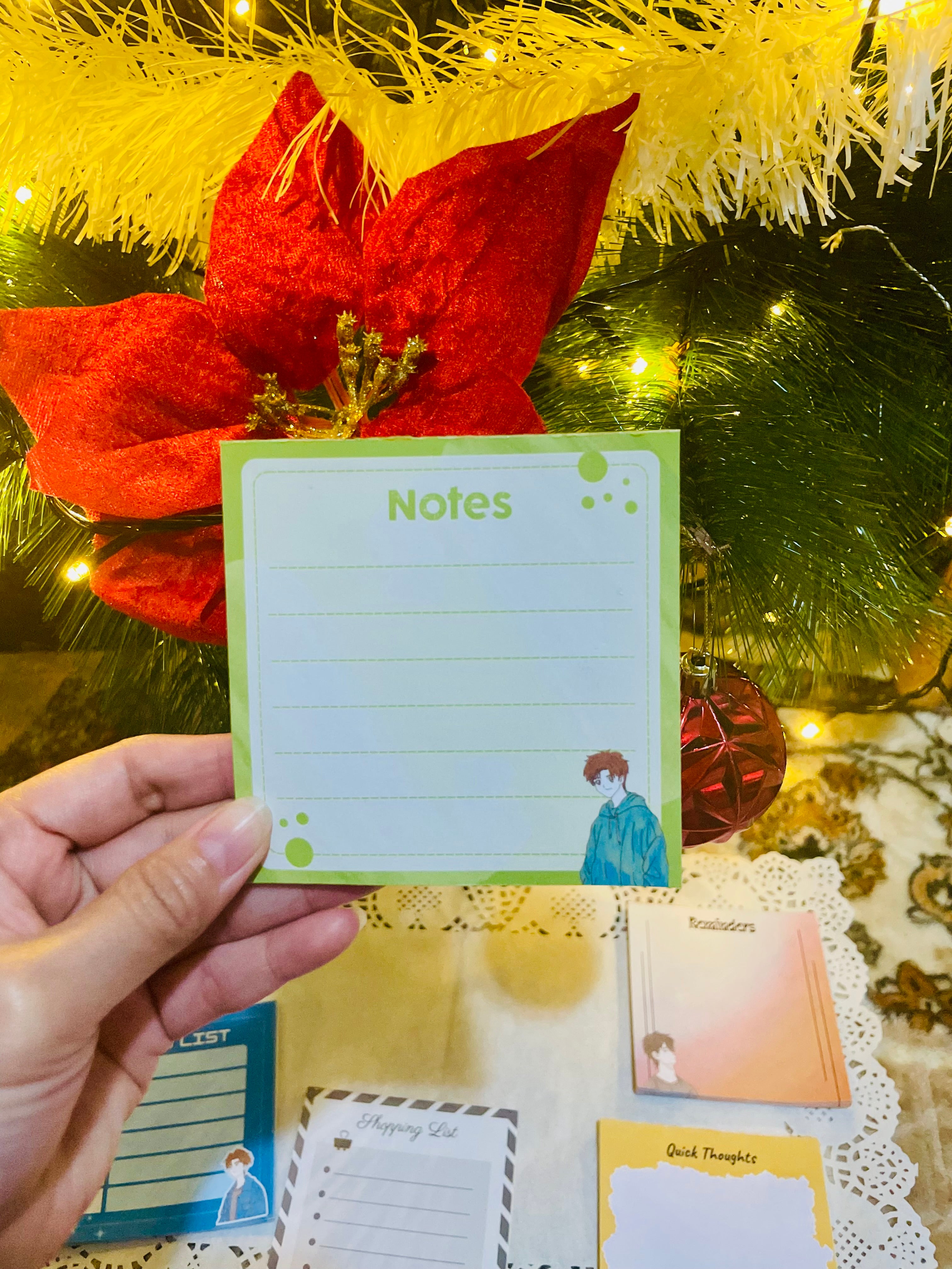 Hand holding a notepad with a Christmas tree and decorations in the background